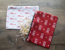 Load image into Gallery viewer, Red and white custom name travel bags laid on a wooden background